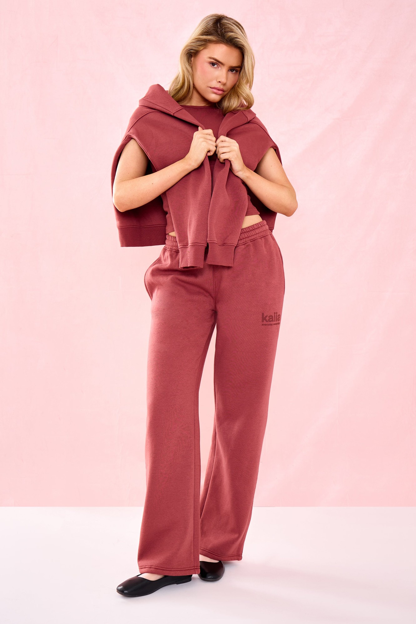 Matte wide-leg joggers in a warm toast color, featuring an elastic waistband and subtle "kaiia" slogan, styled with a matching cropped hoodie draped over the shoulders.