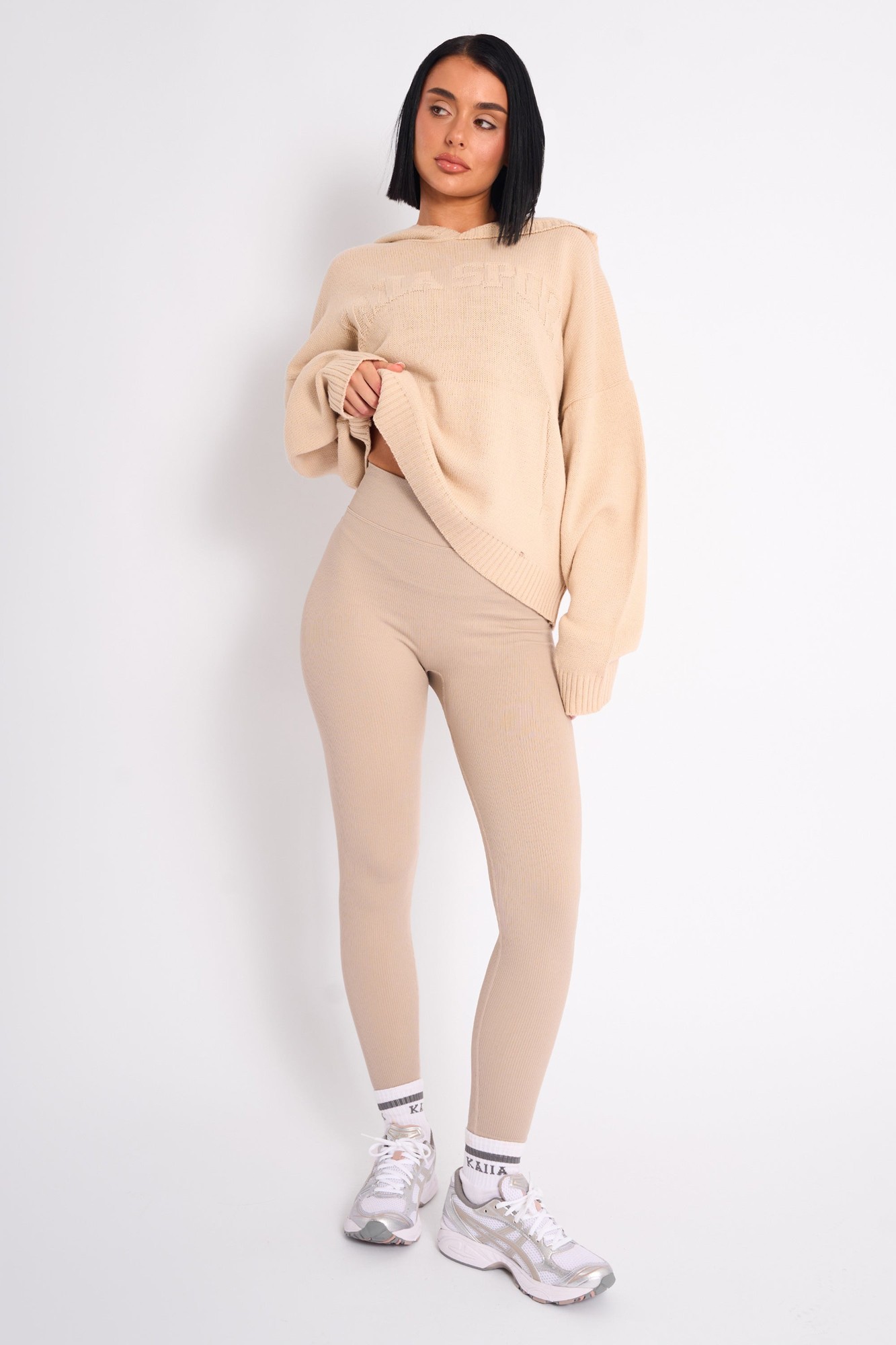 Premium ribbed leggings in a soft stone color, featuring a high-waisted design, paired with a cozy beige sweater and sporty sneakers.