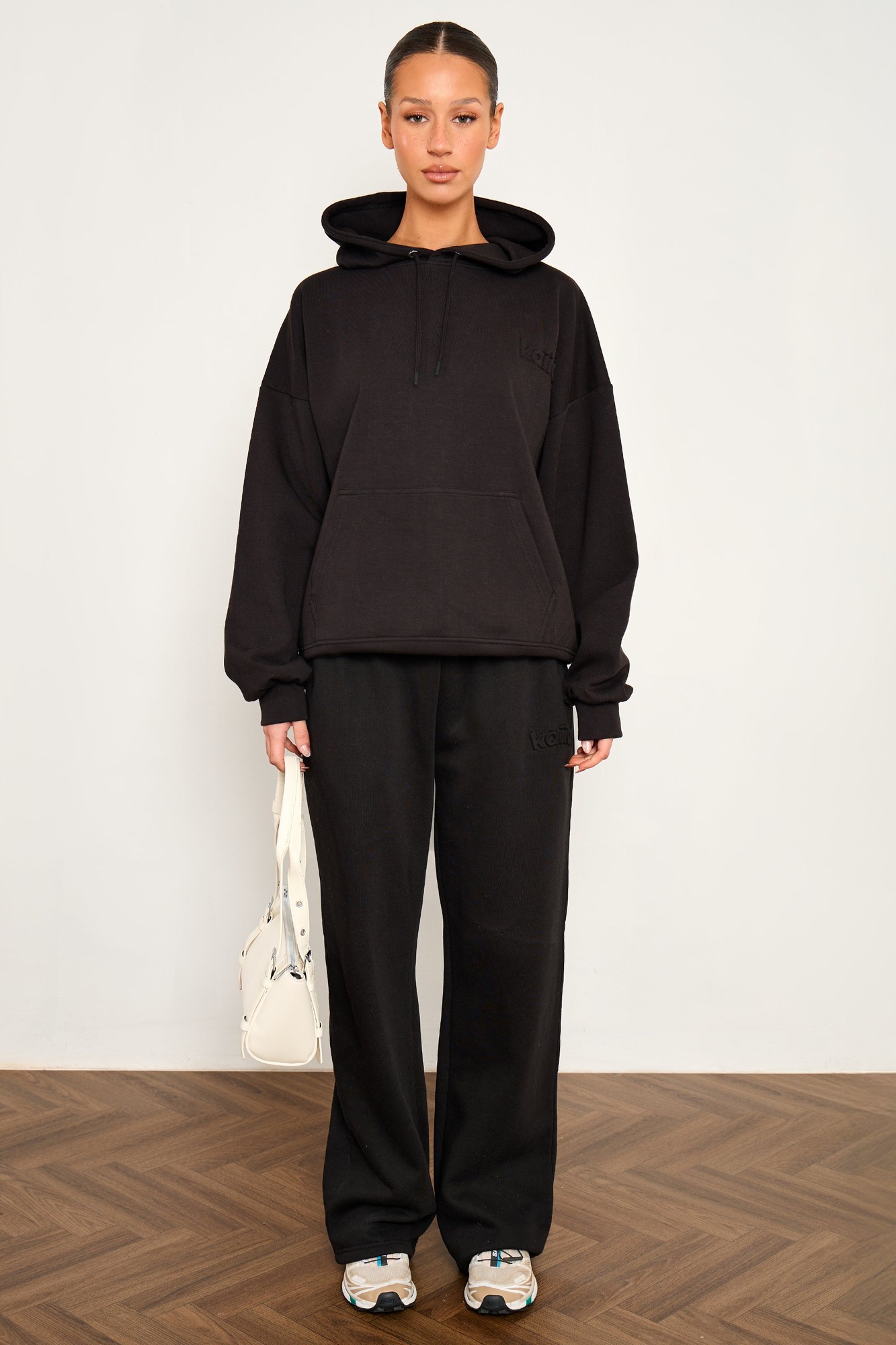 Black wide leg joggers made from premium scuba material, featuring an elastic waistband and a relaxed fit, styled with a matching black hoodie and a white handbag.
