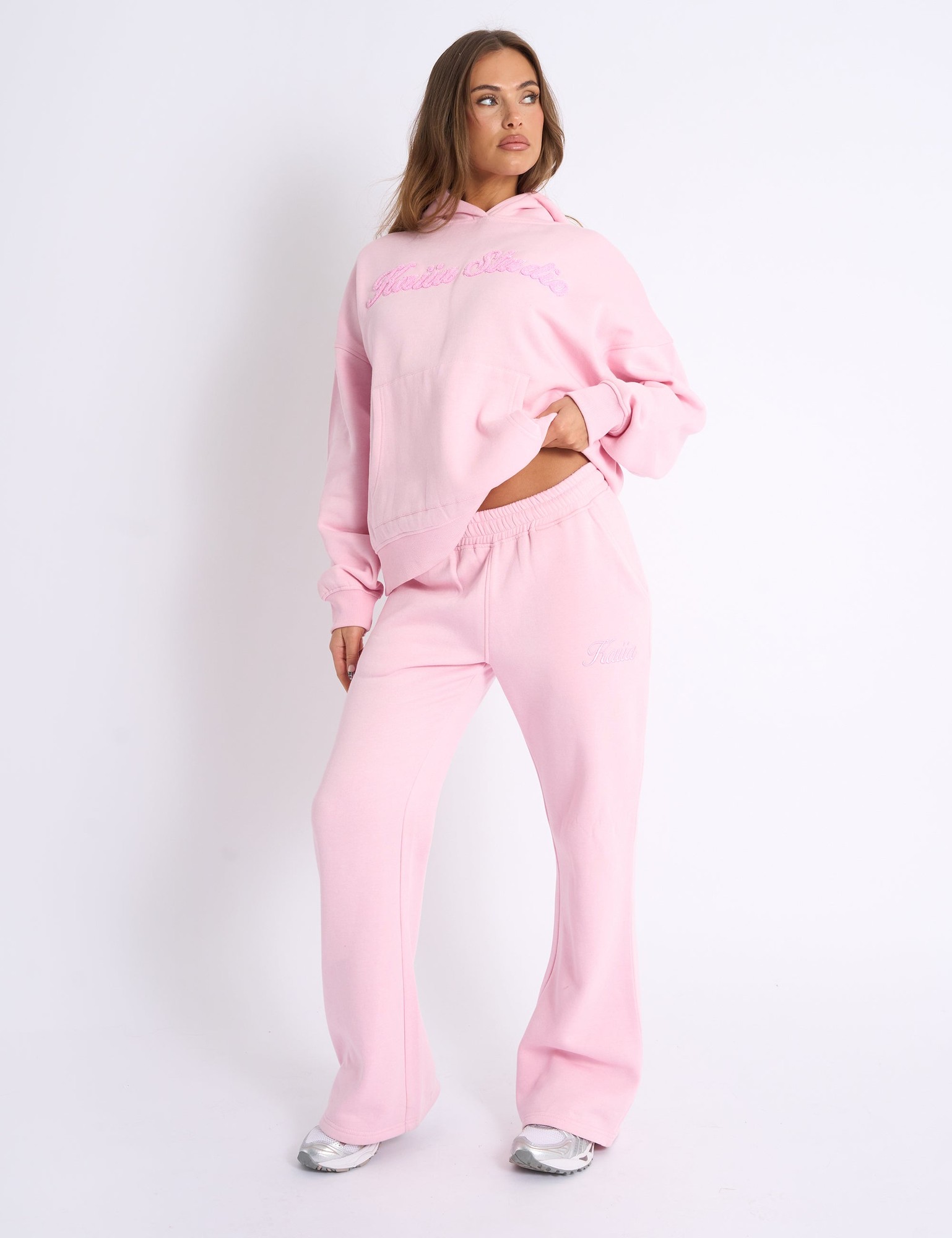 Baby pink wide leg joggers made of soft fabric, featuring a stylish Kaiia script logo on the front, paired with a matching oversized hoodie for a relaxed look.