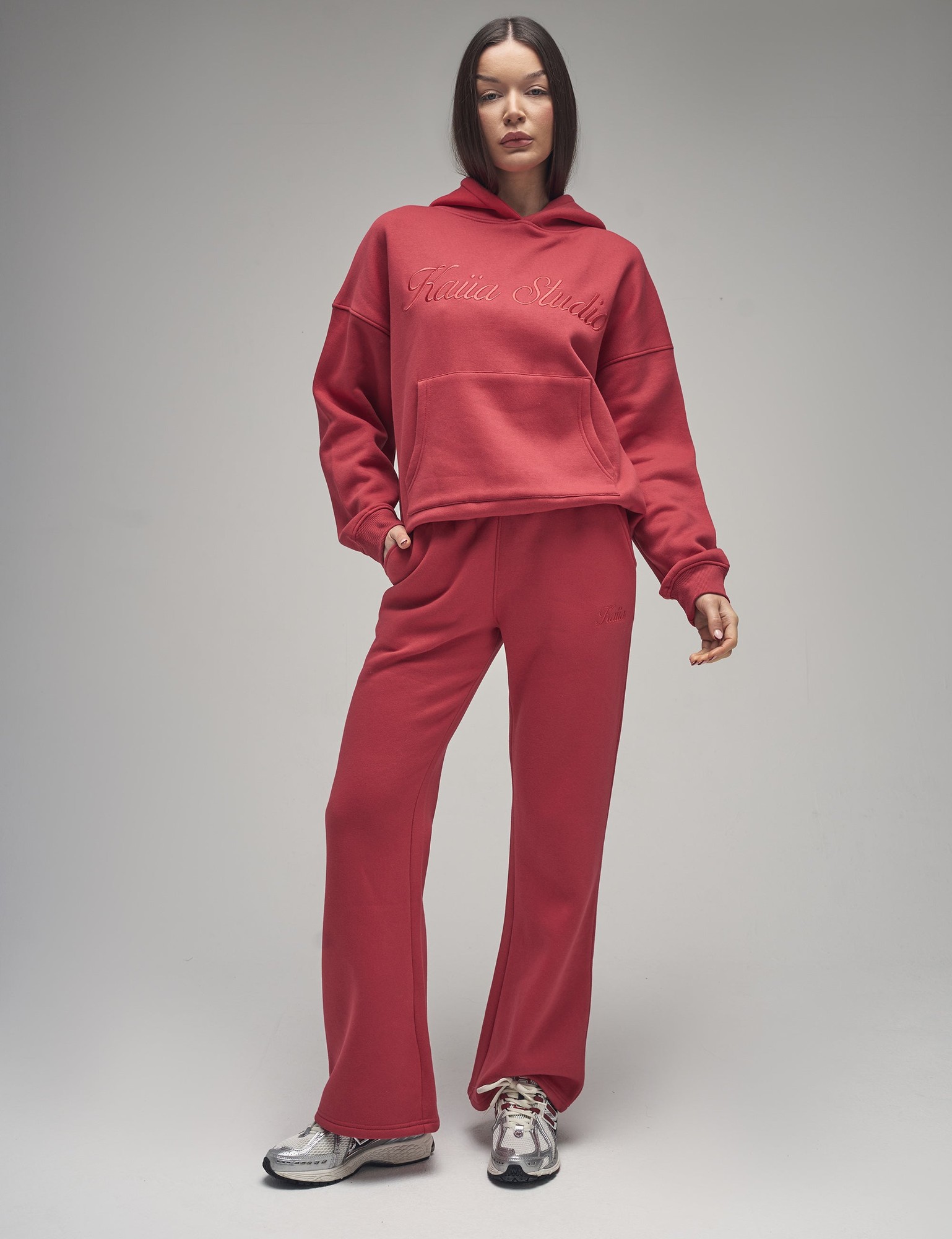Red wide leg joggers made of soft material, featuring a stylish script logo, paired with a matching hoodie, creating a coordinated athletic look.