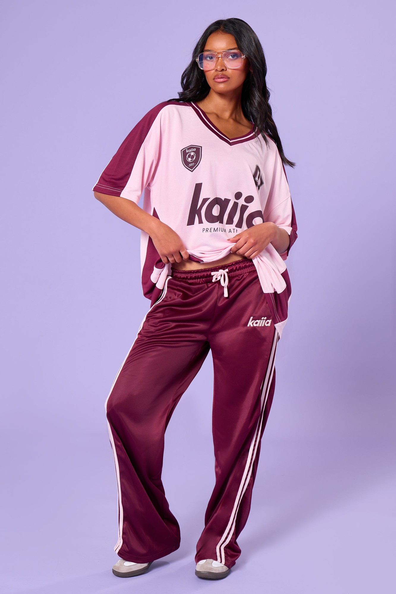 Burgundy and pink tricot joggers featuring side stripes, a relaxed fit, and an elastic waistband, paired with a matching oversized top.