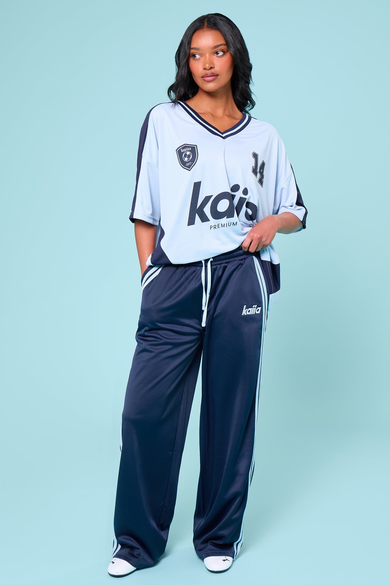 Navy and baby blue tricot joggers featuring side stripes, a relaxed fit, and the Kaiia logo on the left leg, styled with a matching oversized top.