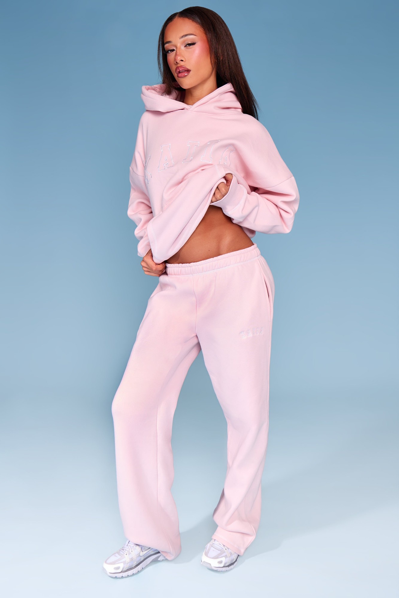 Pink wide-leg joggers with white contrast stitching, featuring an elastic waistband and side pockets, paired with a matching pink hoodie.