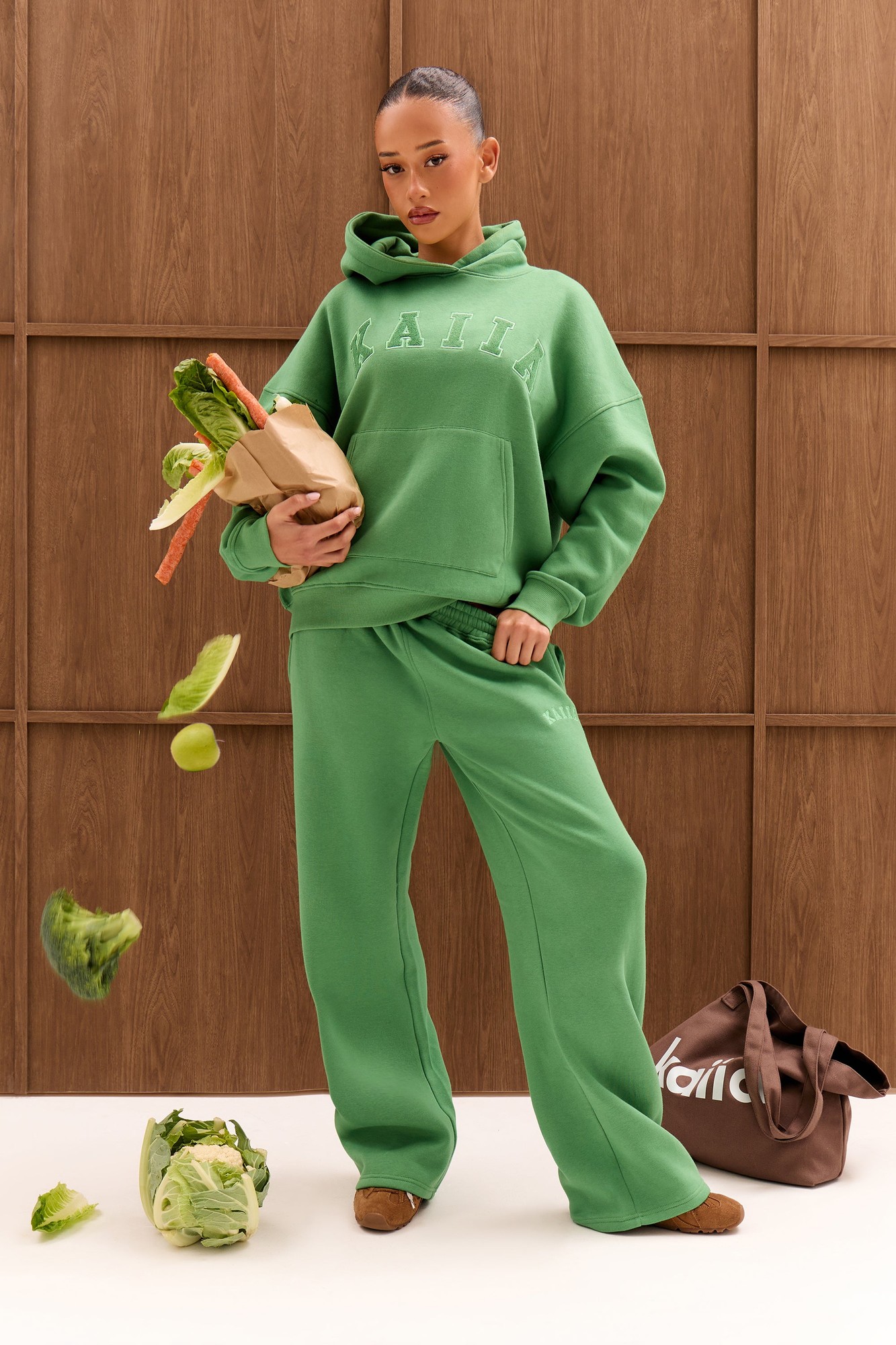 Spring green high-waisted wide-leg joggers made from soft material, featuring a relaxed fit, paired with a matching hoodie, complemented by a stylish tote bag and fresh produce.