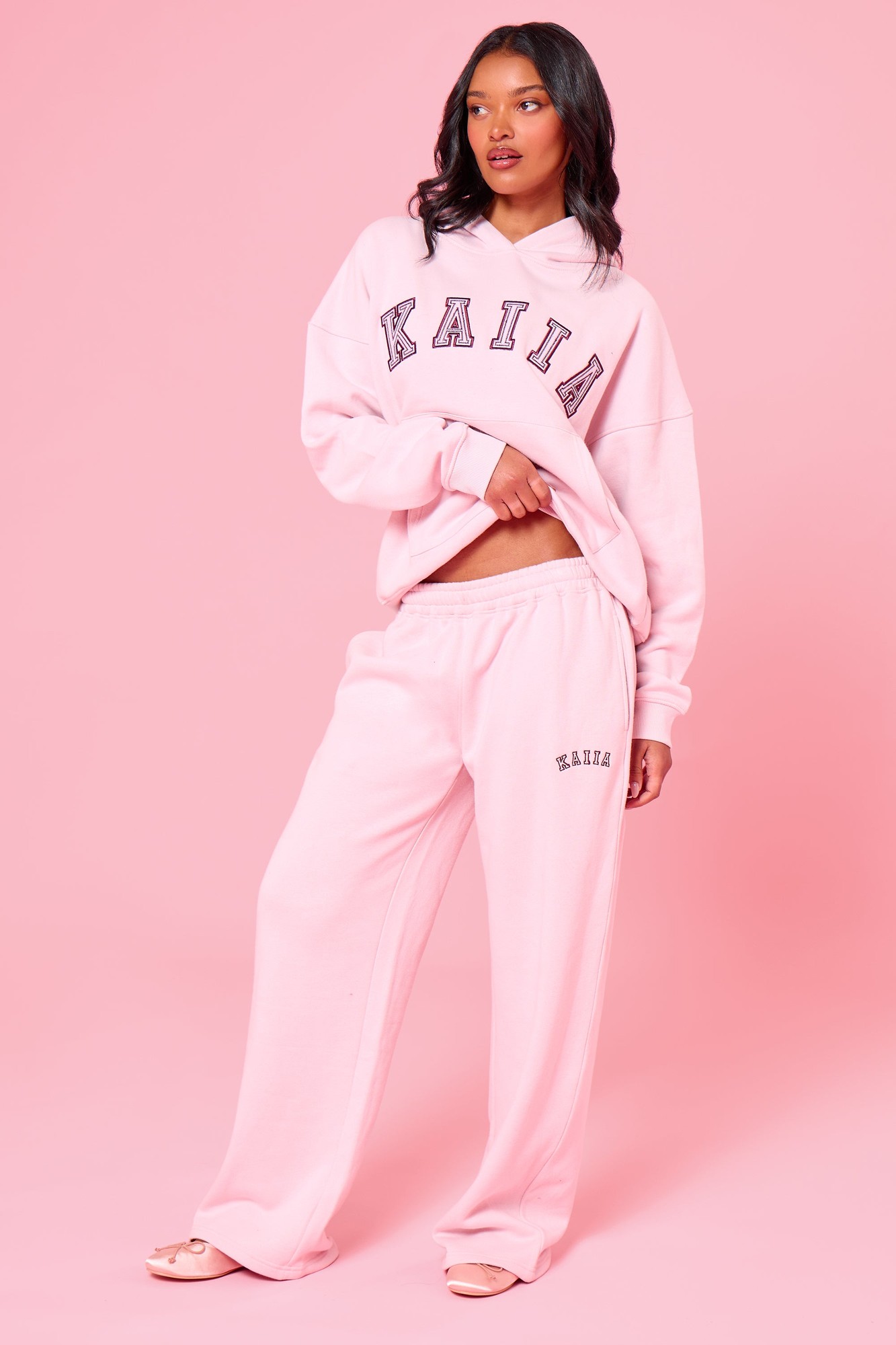 Baby pink wide leg joggers made from soft material, featuring an elastic waistband and the "Kaiia" logo embroidered on the side, styled with a matching oversized hoodie.