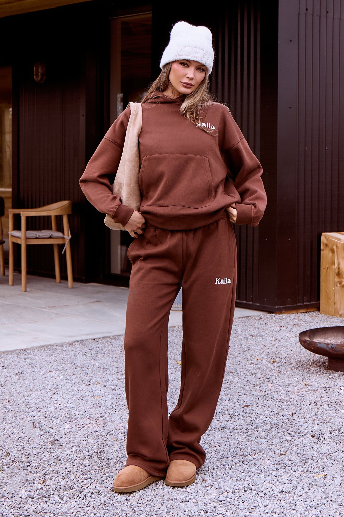 Wide leg joggers in a rich fudge color, made from soft material, featuring an elastic waistband and subtle branding on the side, styled with a matching hoodie and winter hat.