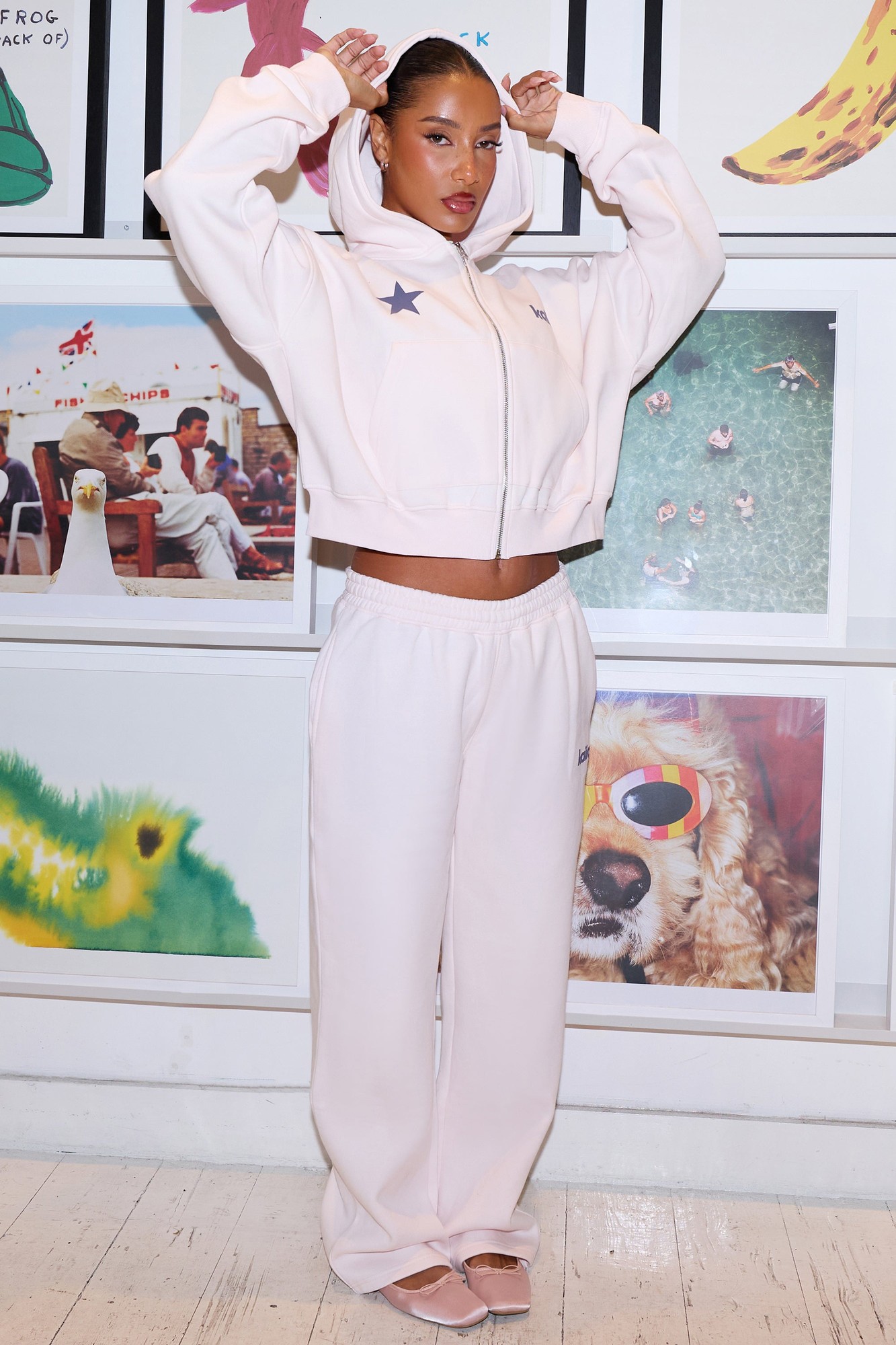 Shell pink wide leg joggers with dark grey star detail, made from soft material, paired with a matching cropped hoodie, styled with a confident pose against a colorful backdrop.