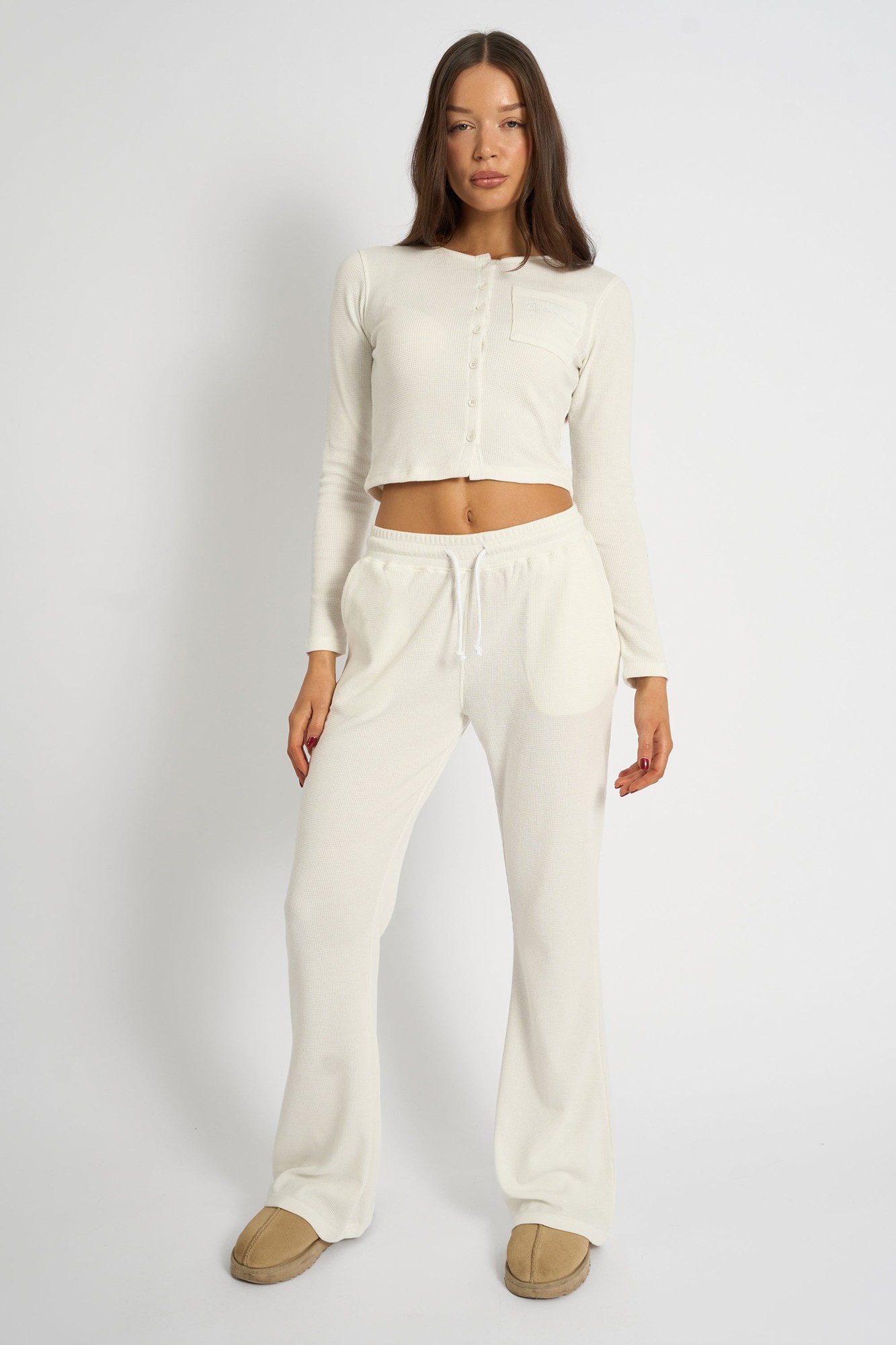 Cream-colored waffle knit wide leg joggers with a drawstring waist, paired with a matching long-sleeve cropped top, styled with cozy slippers.