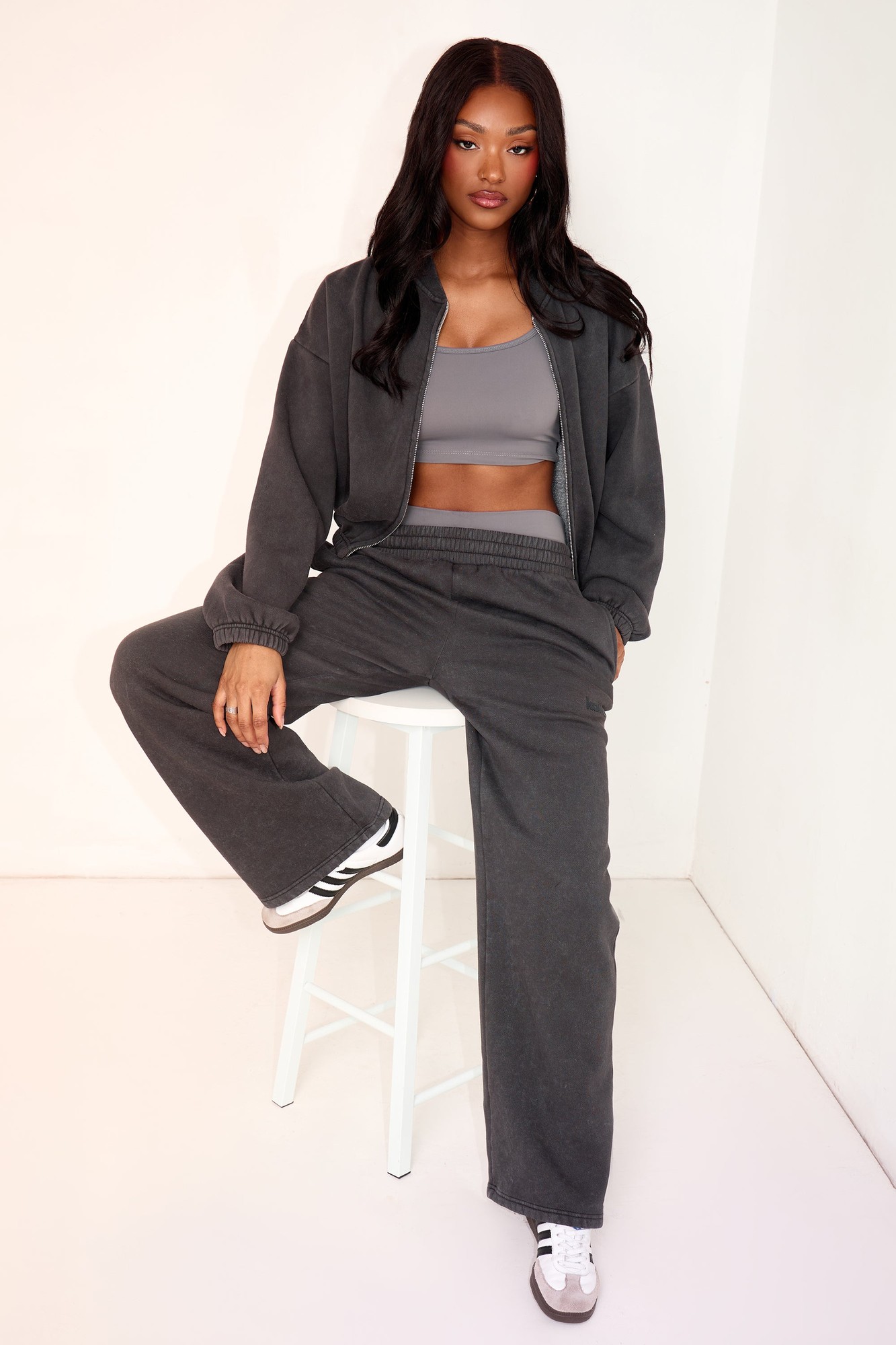 Wide leg joggers in washed black, featuring a relaxed fit and elastic waistband, paired with a matching cropped jacket and gray sports bra, styled with white sneakers.