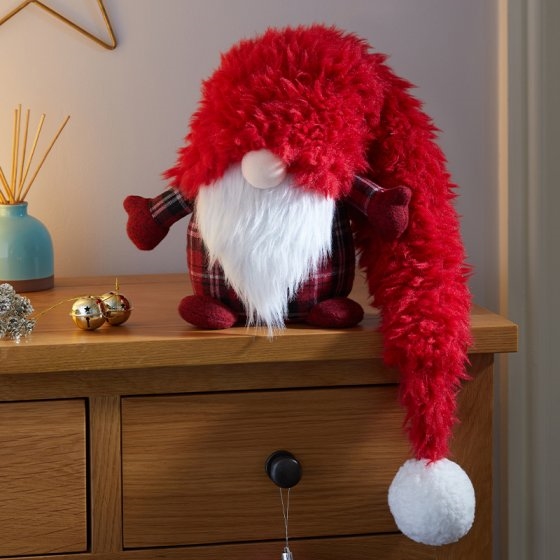Super fluffy winter wolf figure with a red furry body, plaid arms, a white beard, and a long red hat ending in a white pom-pom, sitting on a wooden surface.