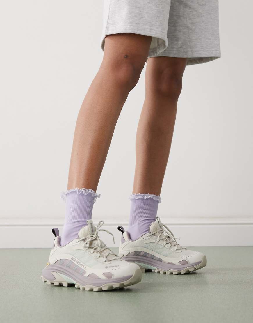 Light greige Merrell Moab Speed 2 GORE-TEX hiking boots with a mesh upper, cushioned sole, and purple accents, paired with ruffled lavender socks and grey shorts.
