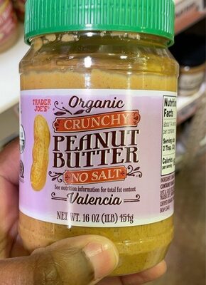 Organic crunchy peanut butter in a clear jar with a green lid, featuring a pink label that reads "Peanut Butter No Salt" and a peanut graphic, 16 oz size.