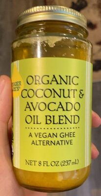 Glass jar with a gold lid containing a yellowish oil blend, labeled "Organic Coconut & Avocado Oil Blend" with a green background and vegan ghee alternative text.