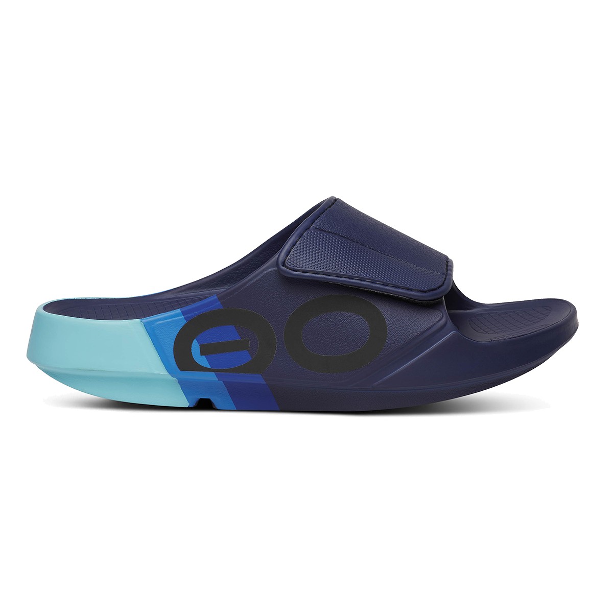 Navy blue recovery slides with a velcro strap, featuring a bold black circle logo and a light blue accent on the heel, designed for comfort and support.