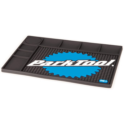 Black rubber mat with a textured surface, featuring a blue gear graphic and "Park Tool" logo, multiple compartments for tools, and a circular area for small parts.