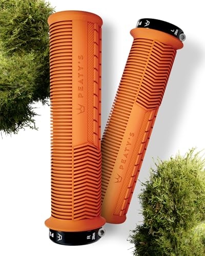 Thick, mango-colored rubber grips with textured ridges and a black end cap, featuring the Peaty's logo, set against a backdrop of green moss.