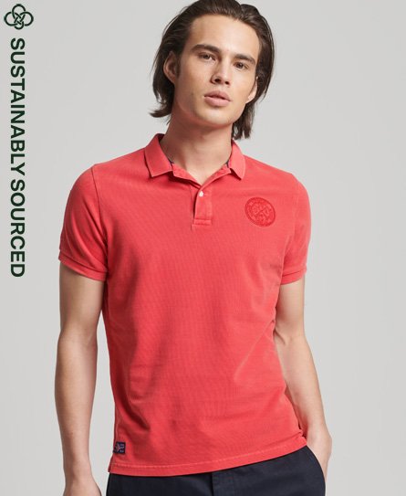 Red polo shirt by Superdry featuring a textured fabric, short sleeves, a classic collar, and a circular logo patch on the chest, labeled as sustainably sourced.