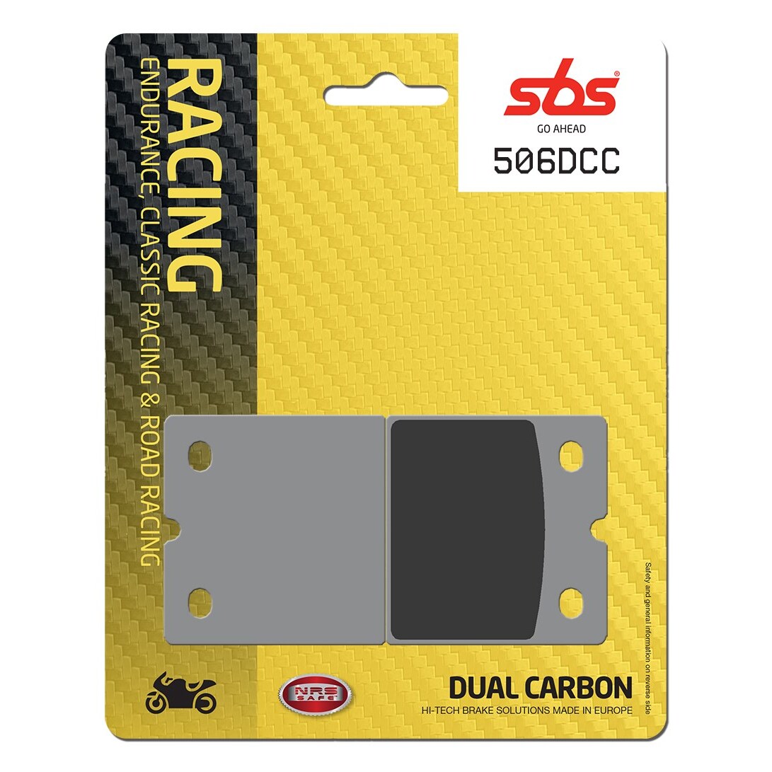 Grey brake pads packaged in a yellow and black card with "RACING" and "DUAL CARBON" text, featuring a carbon fiber pattern background and product code 506DCC.