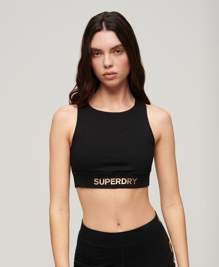 Black sports bra by Superdry, featuring a fitted design, wide straps, and a bold "SUPERDRY" logo in gold across the band.
