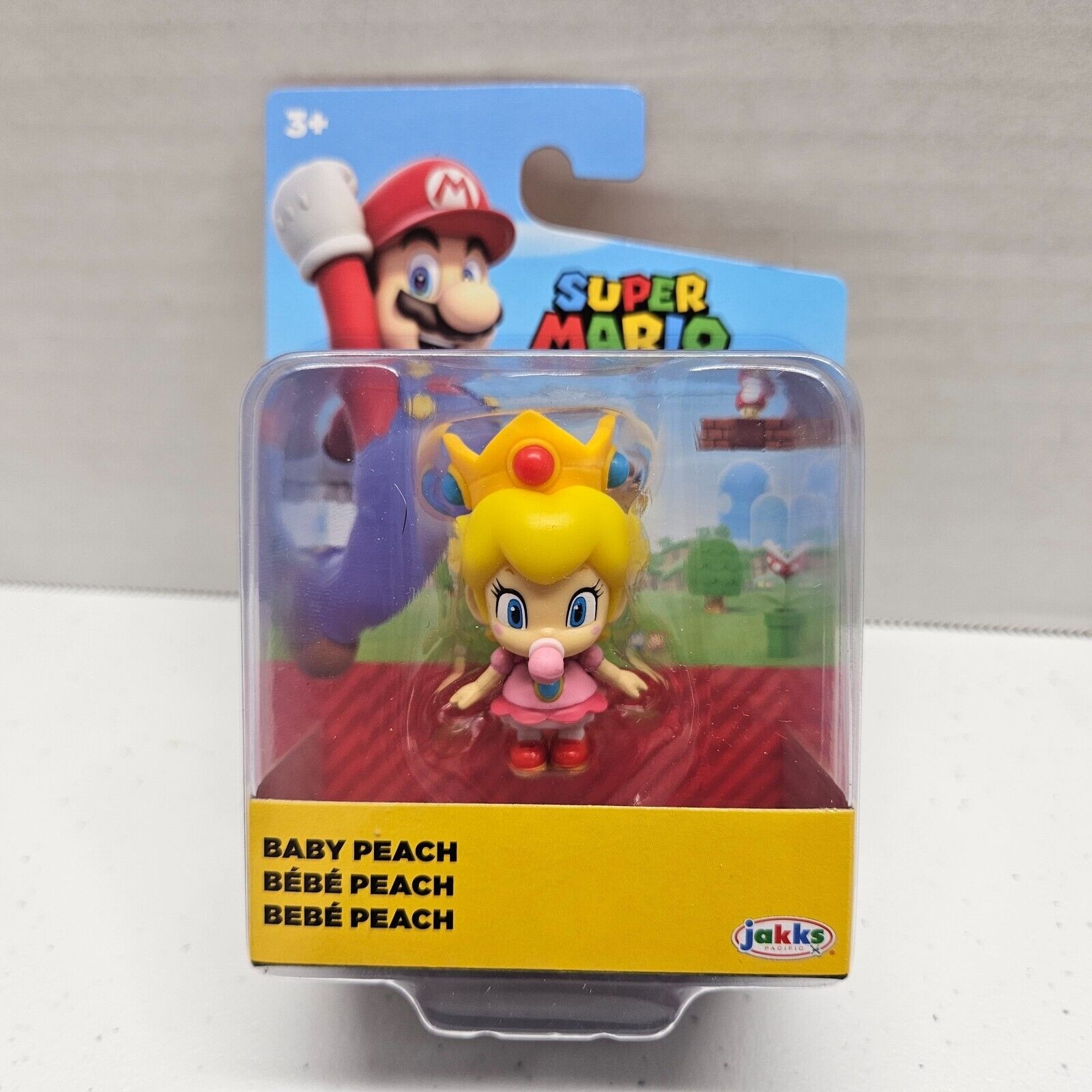 Baby Peach mini figure in a pink dress with a crown, packaged in a clear plastic box featuring Super Mario branding and colorful background graphics.