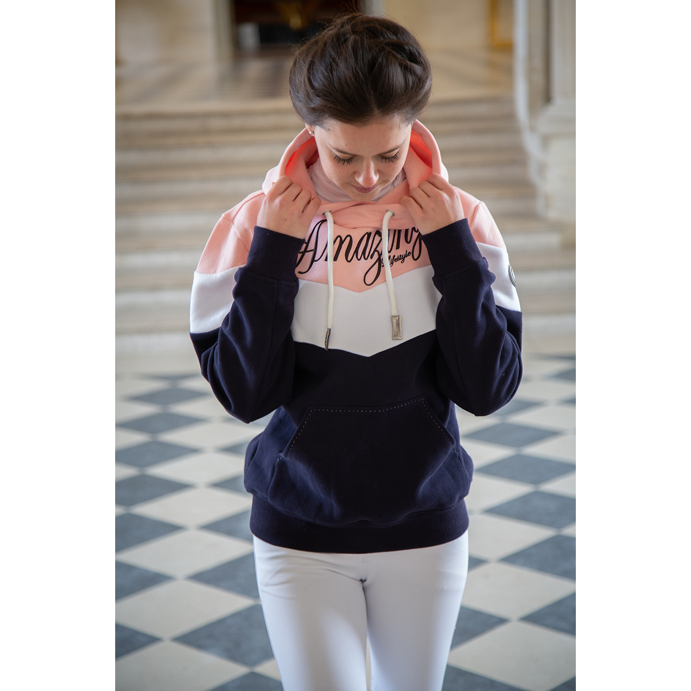 Navy blue and pastel pink color-blocked sweatshirt with a hood, featuring "Amazing" in cursive on the chest and silver drawstrings, styled with white pants.