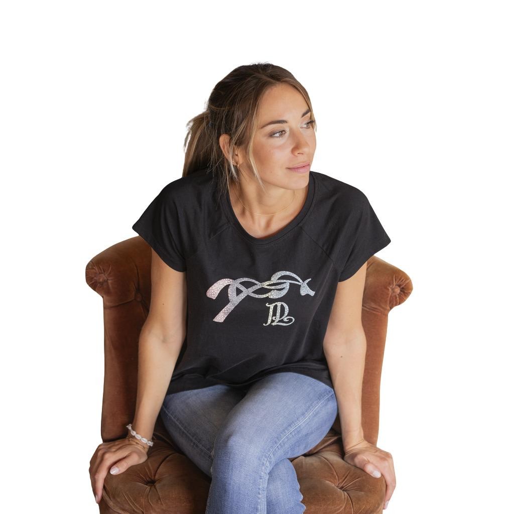 Black T-shirt featuring a funky, glittery design with intertwined letters, made from soft material, paired with light blue jeans and worn by a woman seated on a brown chair.