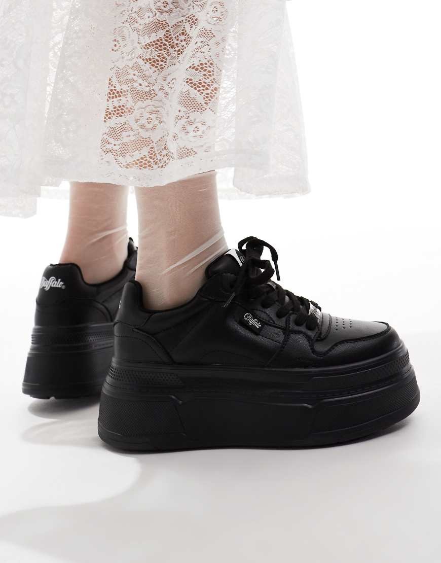 Black platform trainers by Buffalo, featuring a sleek leather upper, lace-up design, and a chunky sole, paired with a white lace dress for a stylish contrast.
