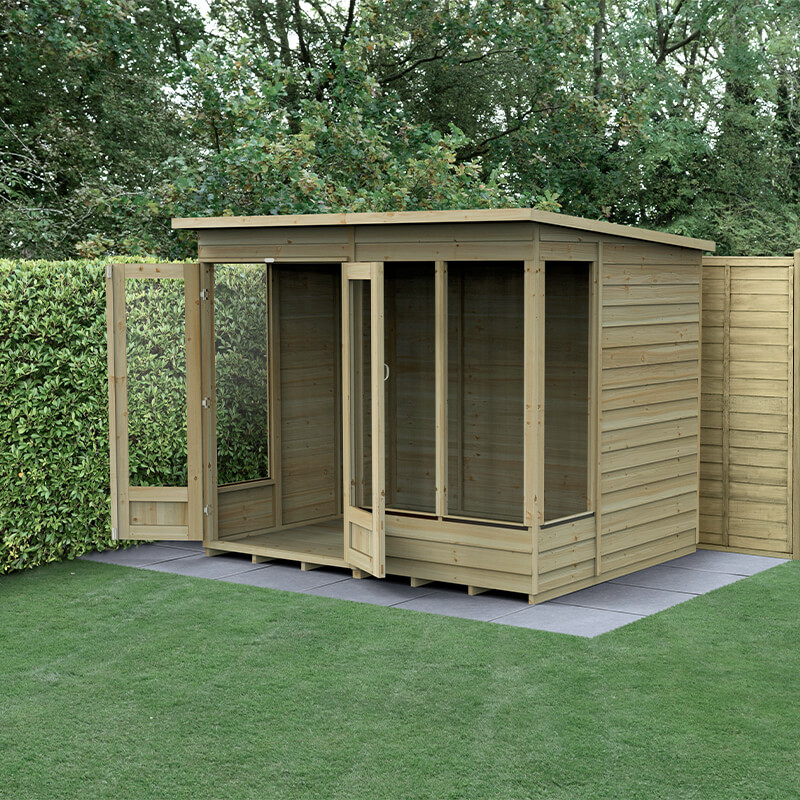 A wooden summer house with a pent roof, featuring double doors and large windows, set on a grassy area surrounded by hedges. The structure is light-colored with a natural finish.