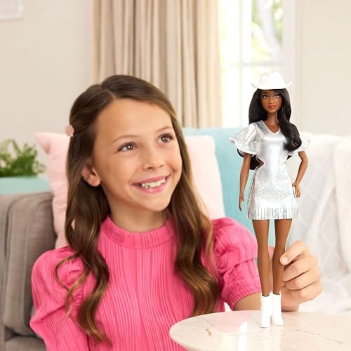 Barbie Fashionistas doll wearing a shiny silver dress with ruffled sleeves, white cowboy hat, and white boots, held by a smiling girl in a pink top.