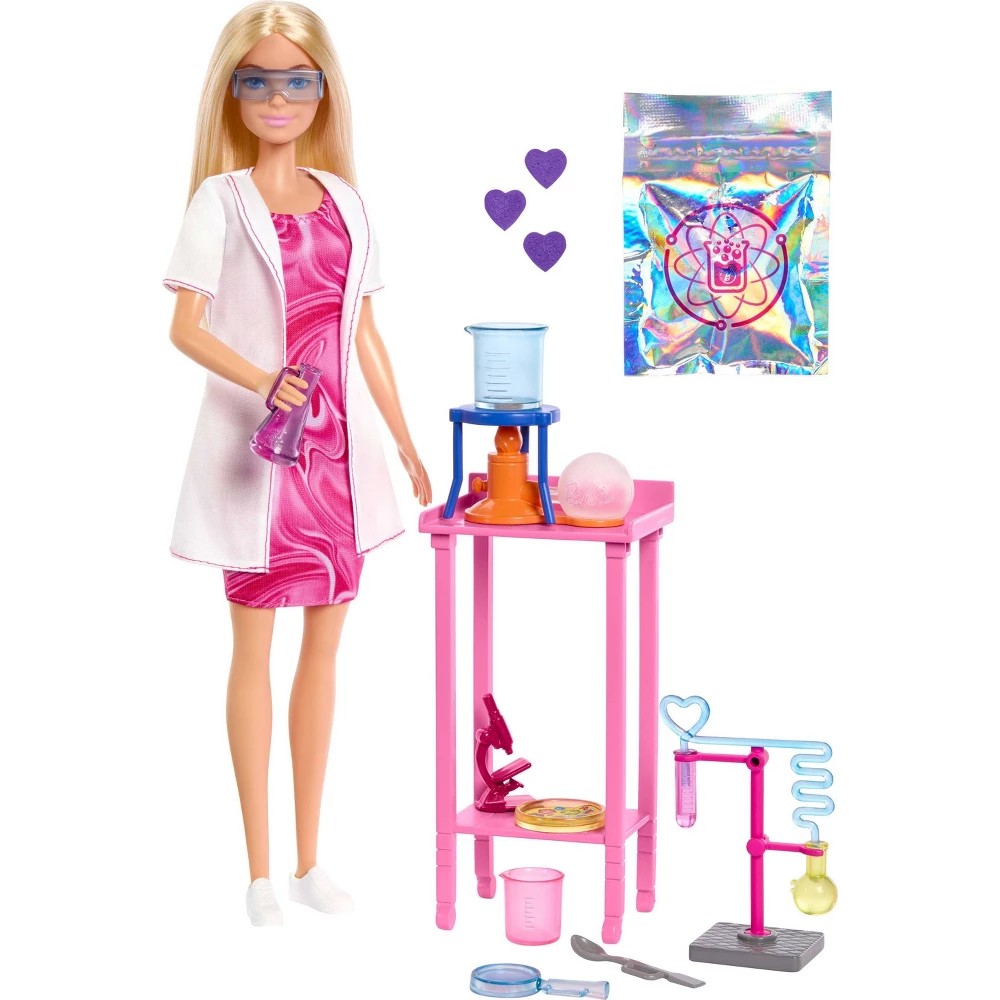 Barbie in a pink and white lab coat with glasses stands beside a pink lab table featuring various colorful scientific equipment and accessories, including beakers and a heart-shaped flask.