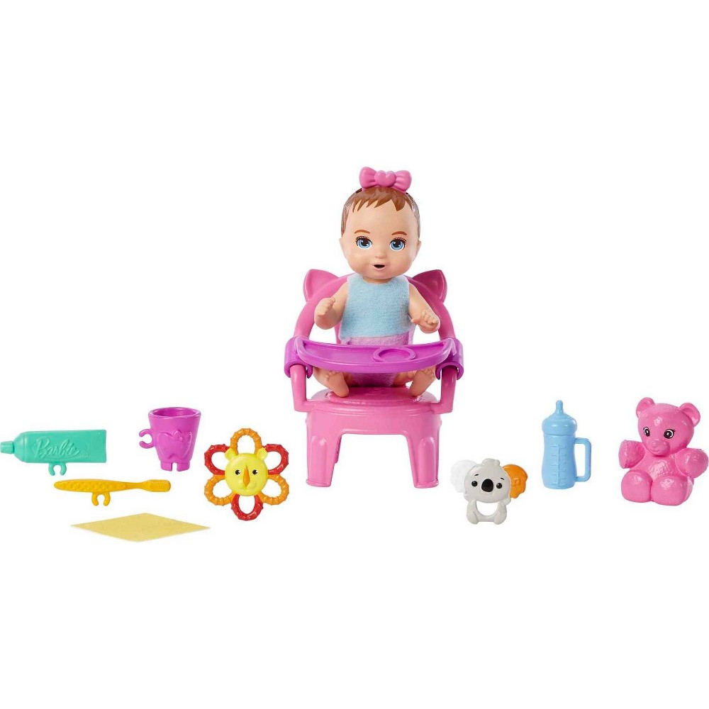 A pink high chair with a seated doll wearing a blue outfit and a pink bow, accompanied by colorful toys including a bear, a flower, a bottle, and a spoon.
