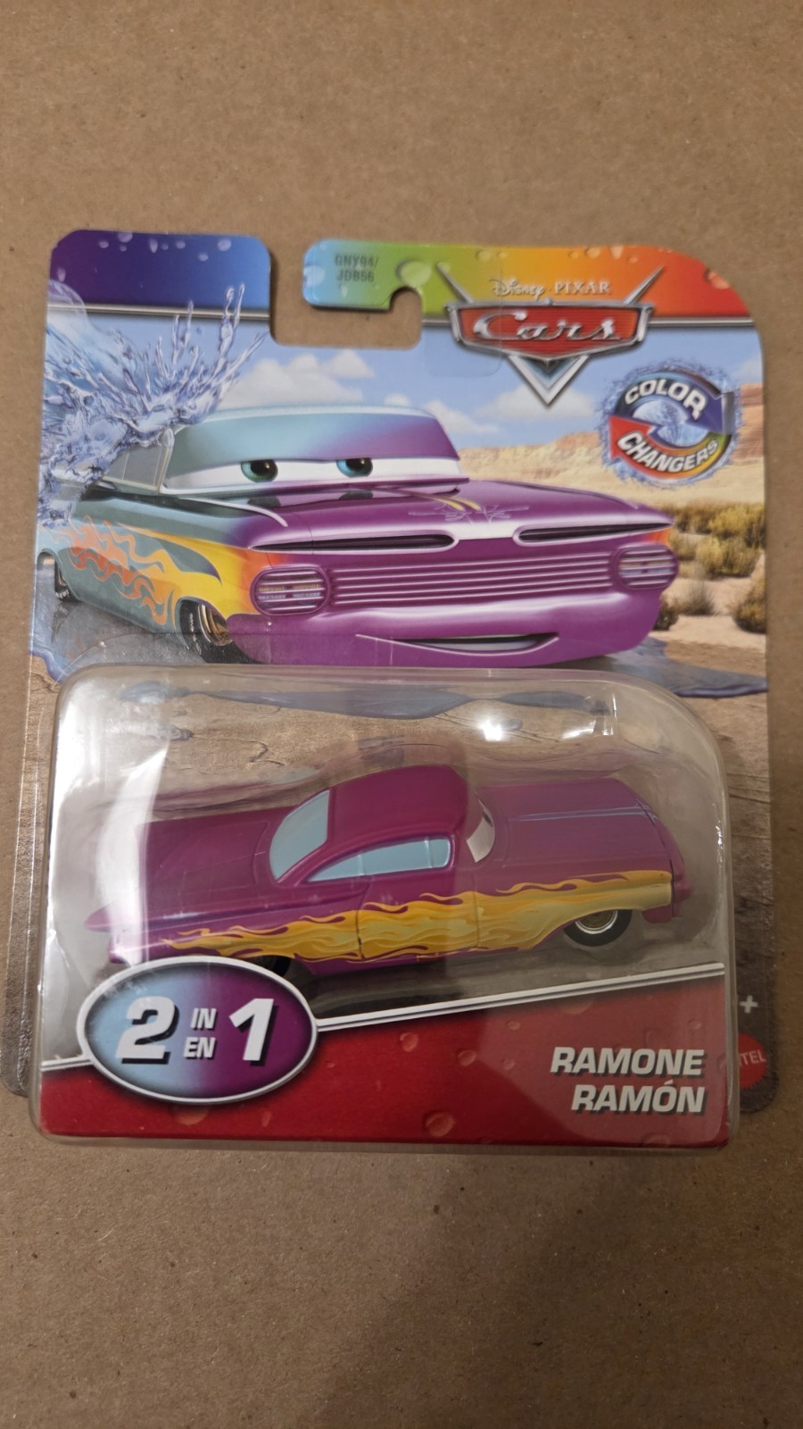 Bright purple and yellow toy car resembling Ramone from Disney's Cars, featuring color-changing capabilities, packaged in a clear plastic blister with a colorful backing.