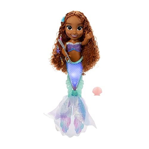 Ariel doll with long, curly brown hair, wearing a shimmering purple and teal mermaid tail, holding a seashell and a trident, with a blue flower accessory in her hair.