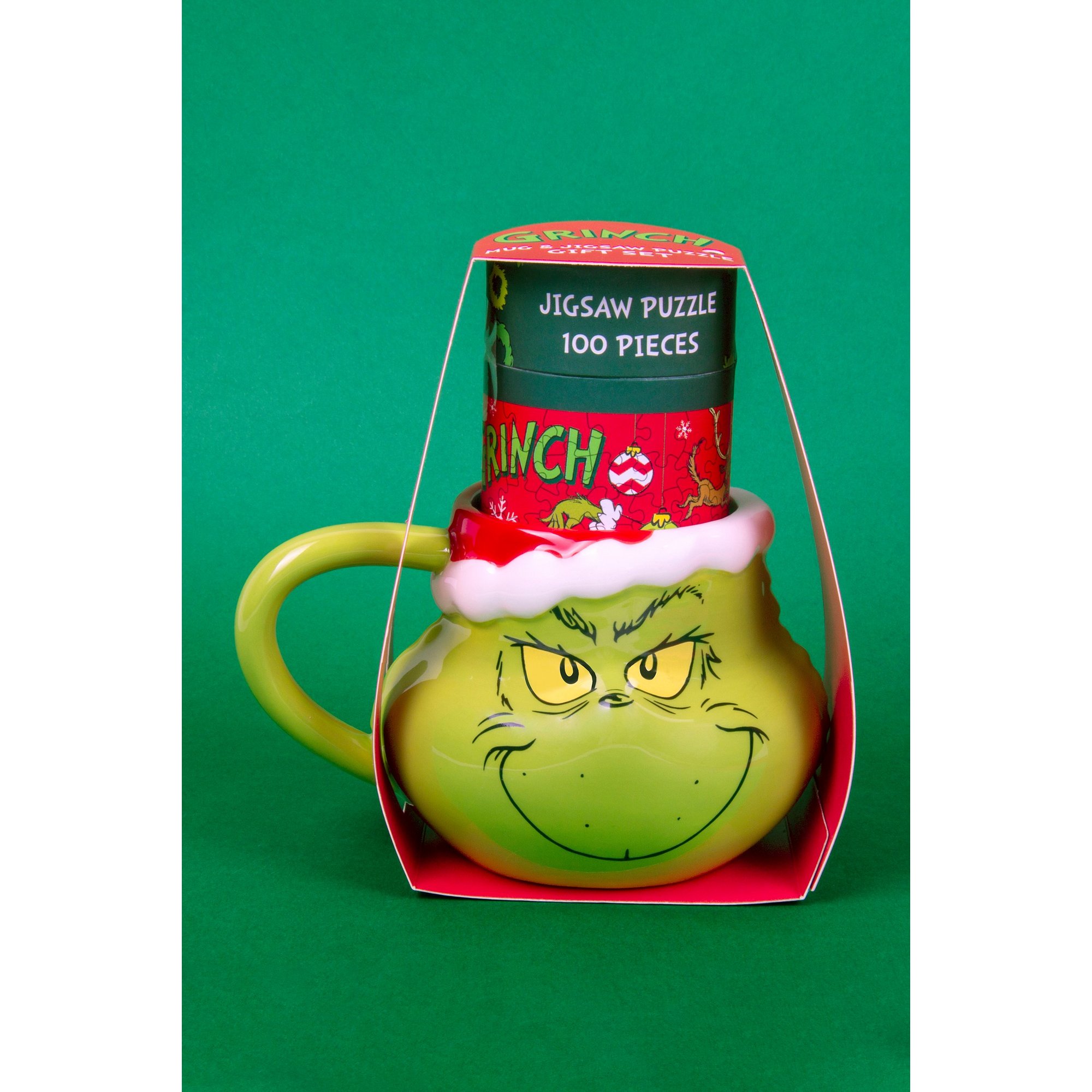 Green ceramic mug shaped like the Grinch's face, featuring a mischievous expression, topped with a red and white puzzle box containing 100 pieces.