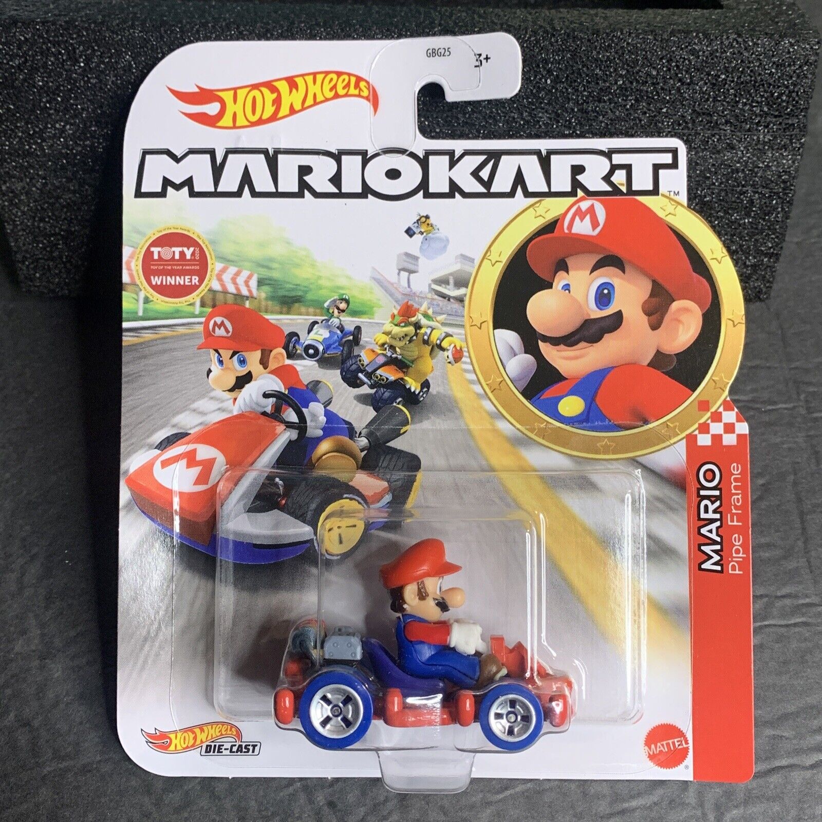 Die-cast Mario Kart vehicle featuring Mario in a red cap and blue overalls, with a red and blue kart, packaged with vibrant graphics and a gold medal emblem.