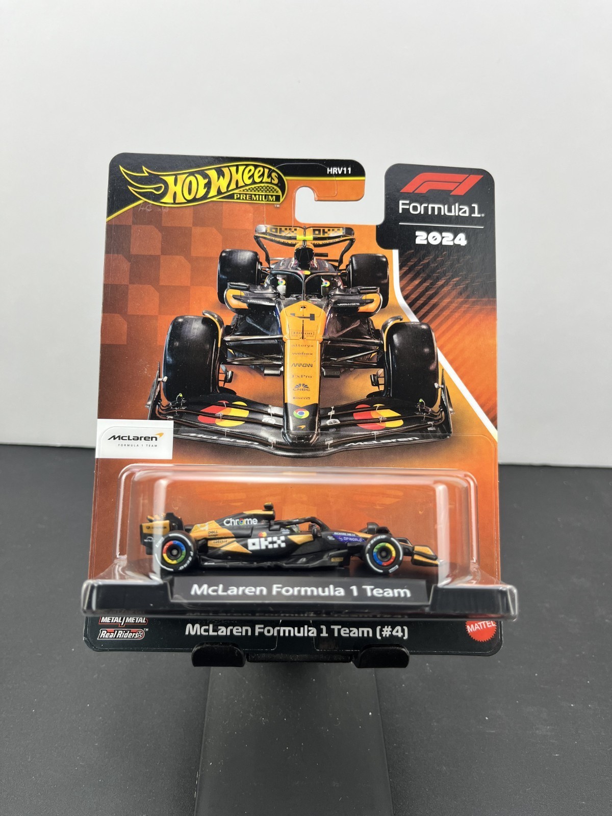 McLaren F1 vehicle by Hot Wheels, featuring a sleek black and orange design, detailed sponsor logos, and rubber tires, displayed on a branded card with a Formula 1 logo.