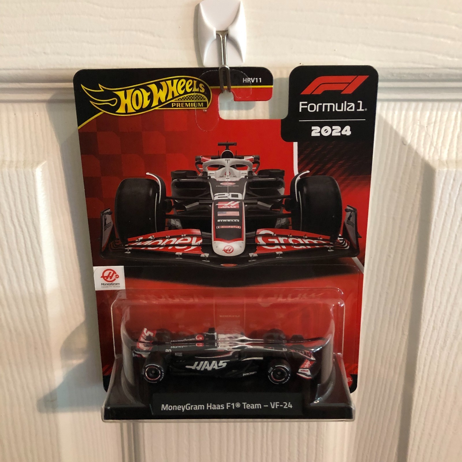 Die-cast model of the Hot Wheels Premium F1 Moneygram Haas car, featuring a sleek black and red design with #20, displayed on a card featuring the F1 logo and team branding.