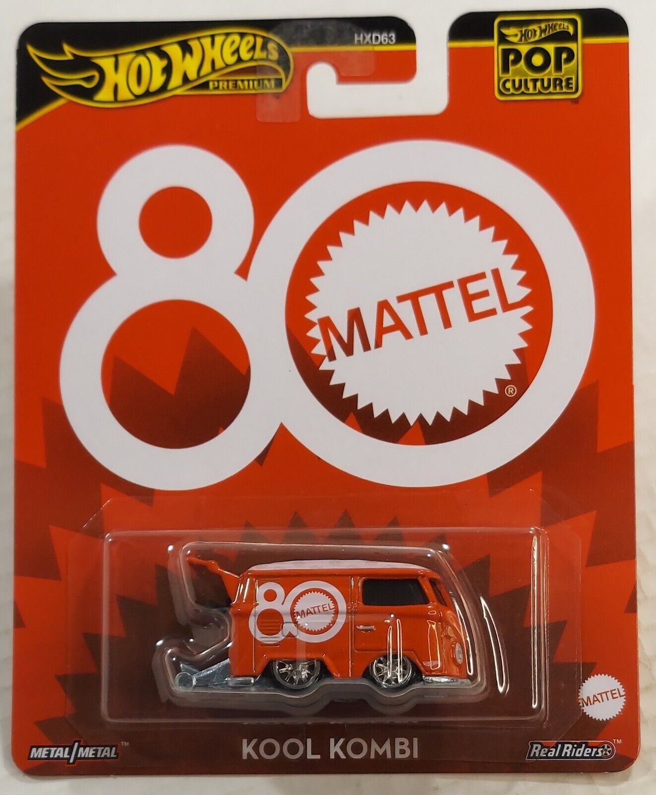Bright orange Volkswagen Kool Kombi die-cast model with white circular logo and "80" design, displayed on a red and white packaging featuring Hot Wheels Premium and Pop Culture branding.