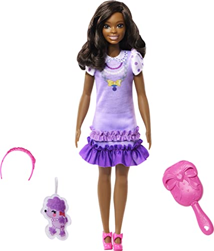 My First Barbie Brooklyn Soft Body Doll features a brown-skinned doll with long dark hair, wearing a purple dress with ruffles, and includes accessories like a pink brush and a headband.