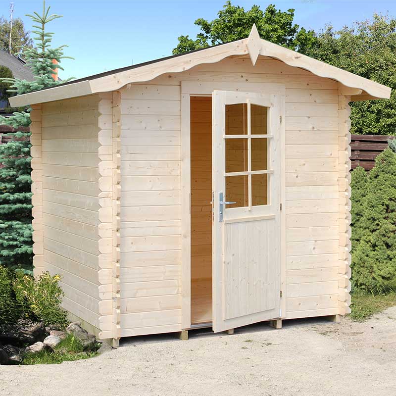 Light-colored wooden log cabin with a peaked roof, featuring a front door with a window and decorative trim, surrounded by greenery and gravel pathway.