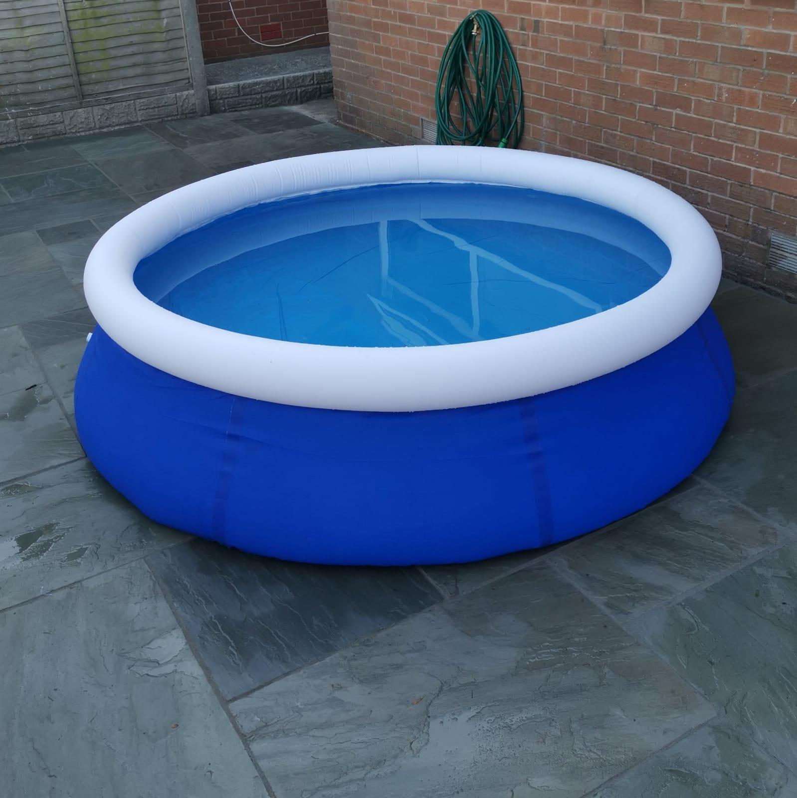Round inflatable paddling pool with a deep blue base and white rim, featuring clear water, set on a stone patio with a brick wall in the background.