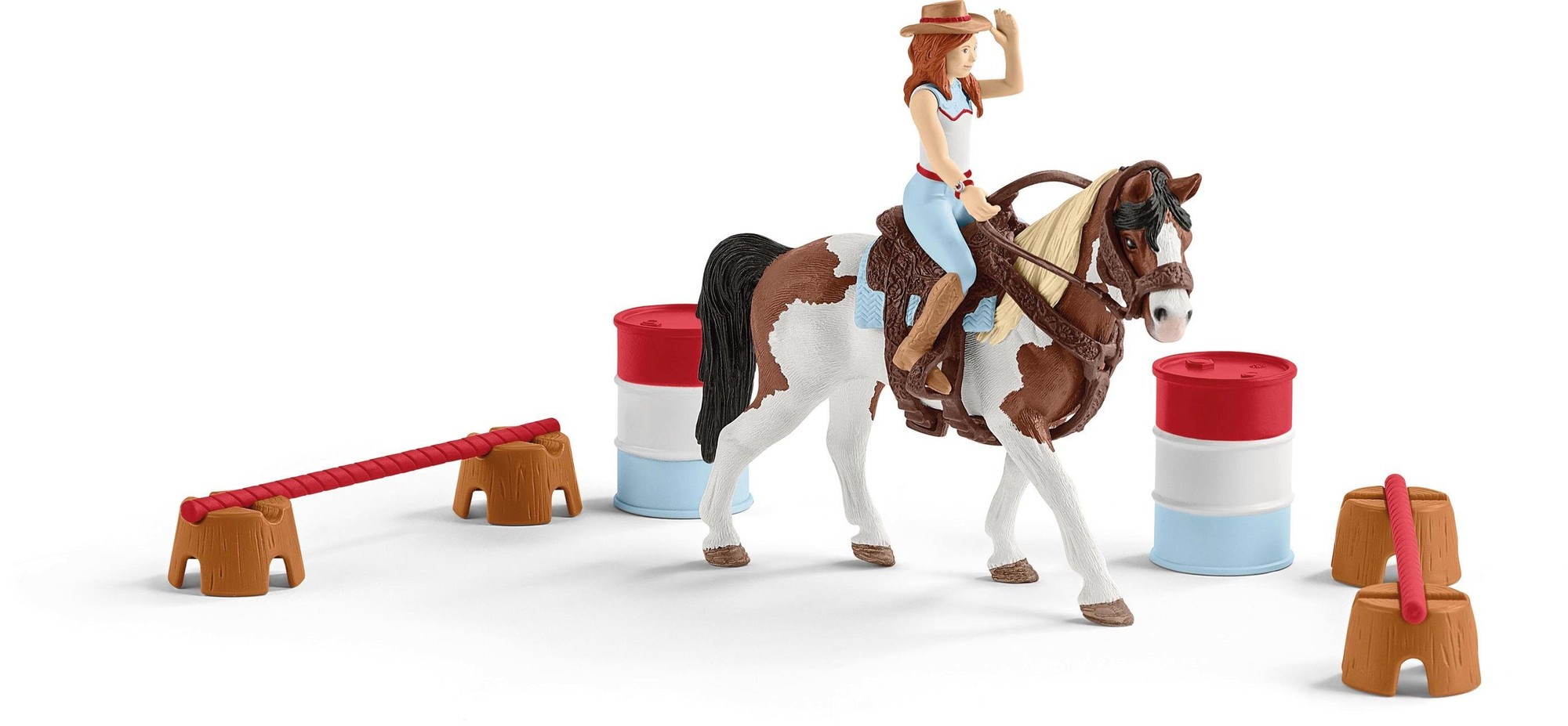 Hannah, a female figure in a cowboy hat, rides a brown and white horse, surrounded by colorful barrels and a jump obstacle in a Western-themed playset.