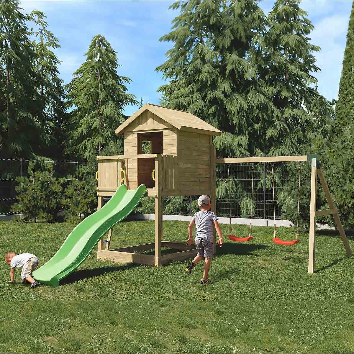 Brown wooden playhouse with a green slide, swings, and a climbing frame, set in a grassy area surrounded by tall trees.
