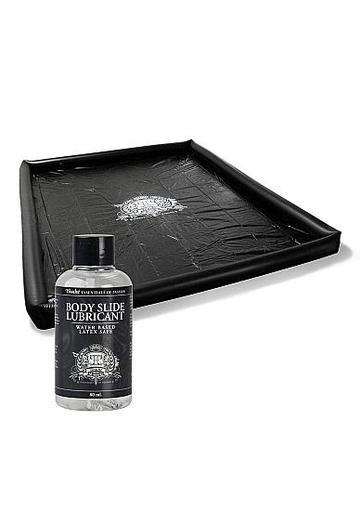 Black rectangular play mat with raised edges, made of smooth material, accompanied by a bottle of water-based lubricant featuring a black label and silver design.