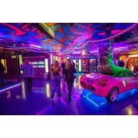 Colorful indoor crazy golf venue with neon lights, vibrant murals, and a pink car obstacle.