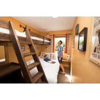Themed hotel room with wooden bunk beds, orange walls, and framed pictures; child in striped shirt looking out window.