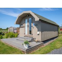 Beige wooden cabin with arched roof, glass doors, and small deck on grassy lawn.