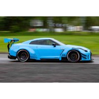 Blue sports car with black wheels and large rear spoiler, driving fast on a road with blurred green background.