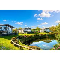 Holiday park with modern cabins, lush greenery, pond, and blue sky; ideal for family stays and entertainment.